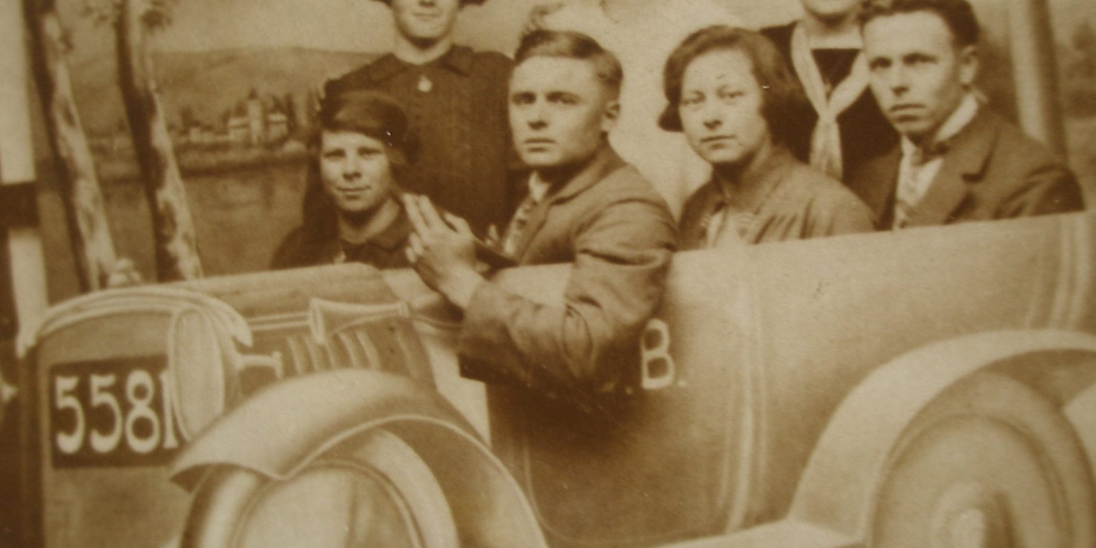 Several people crowded into an open topped car in an old photograph