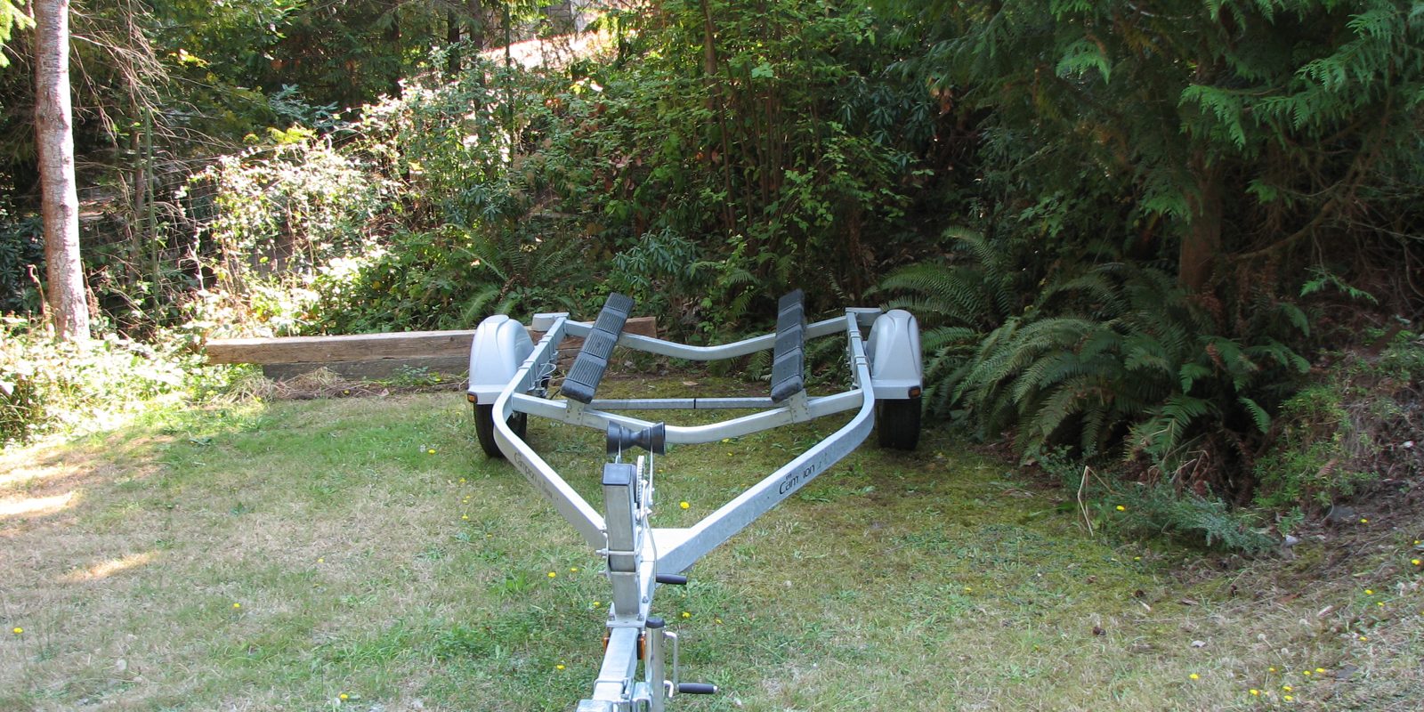 An empty boat trailer on grass, its coupling and jockey wheel visible