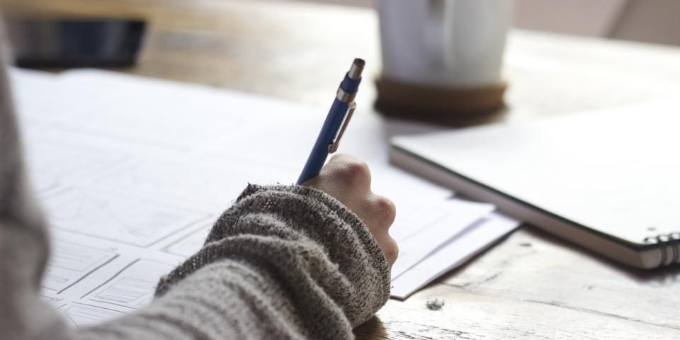 A hand writing notes at a desk beside a mug of coffee